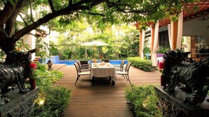 A wooden pathway leading to a table set for dining, surrounded by greenery and statues. - Baan Klang Wiang Boutique Hotel Chiang Mai (Chiang Mai)