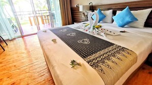Une chambre d’hôtel avec un grand lit, un plancher en bois, une vue sur l’extérieur à travers des portes vitrées et une table de chevet avec une lampe.