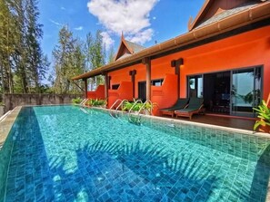 Une piscine à l’eau d’un bleu cristallin, entourée d’un bâtiment à la façade rouge et au toit recouvert de tuiles.