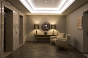 Un lobby moderno con una lámpara de techo, dos lámparas de pared, un adorno circular, un banco de madera y una silla.