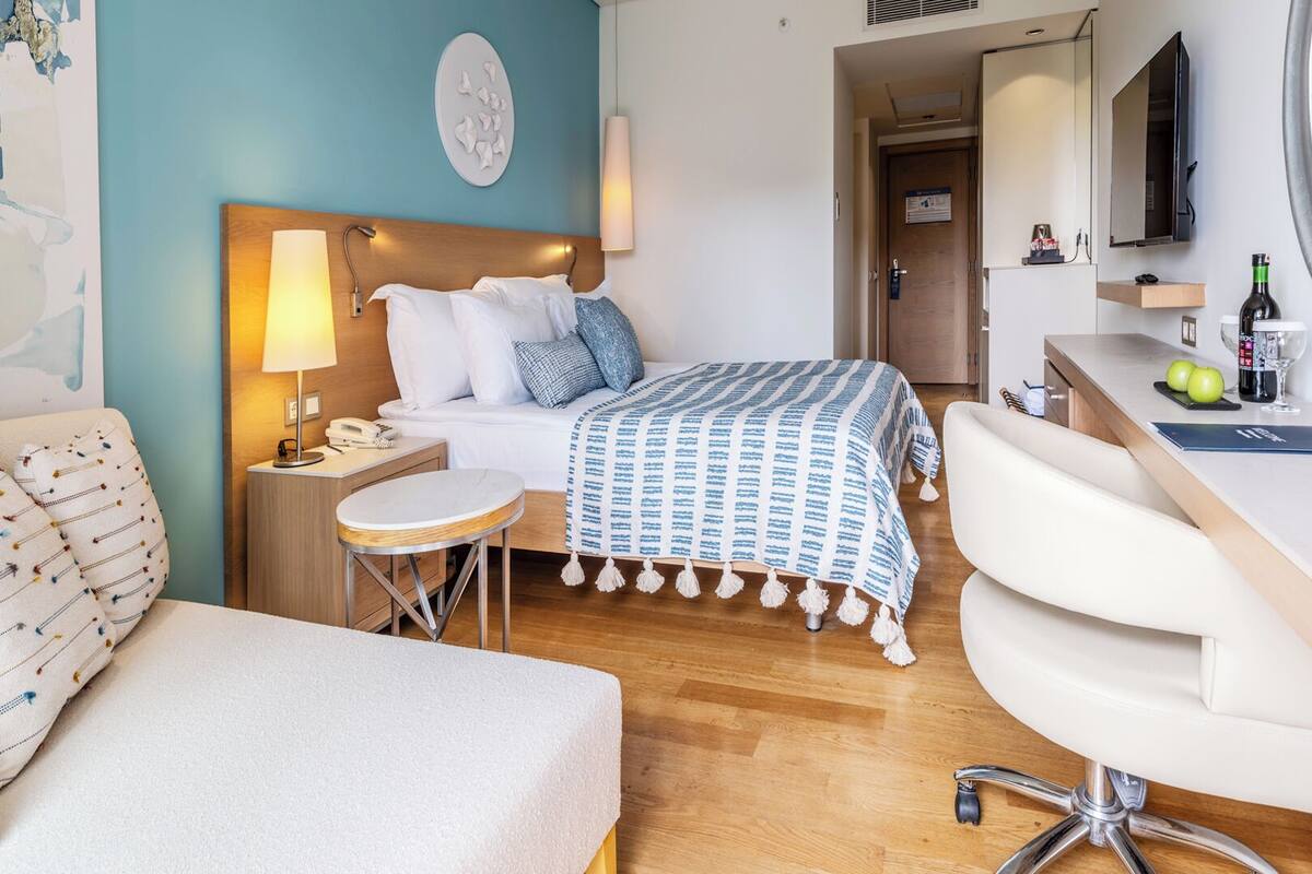 A modern hotel room with a bed, a desk, a chair, and a small table.