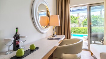 Habitación de hotel con encimera de mármol, espejo redondo, lámpara, botella de vino, copas y manzanas.
