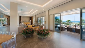 Un vestíbulo amplio con zona de recepción, asientos y grandes ventanales con vistas al mar.