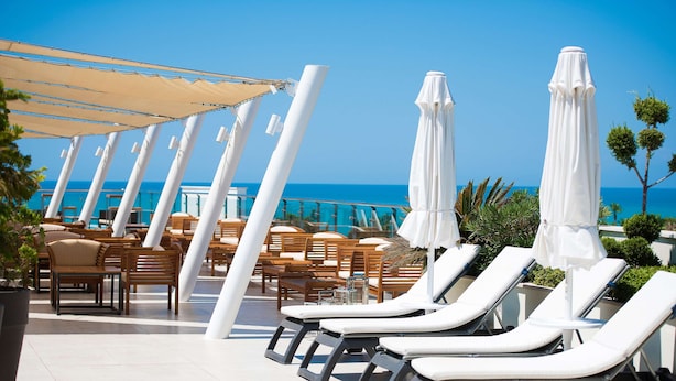 Zona de piscina con sillones y sombrillas, con vistas al mar.