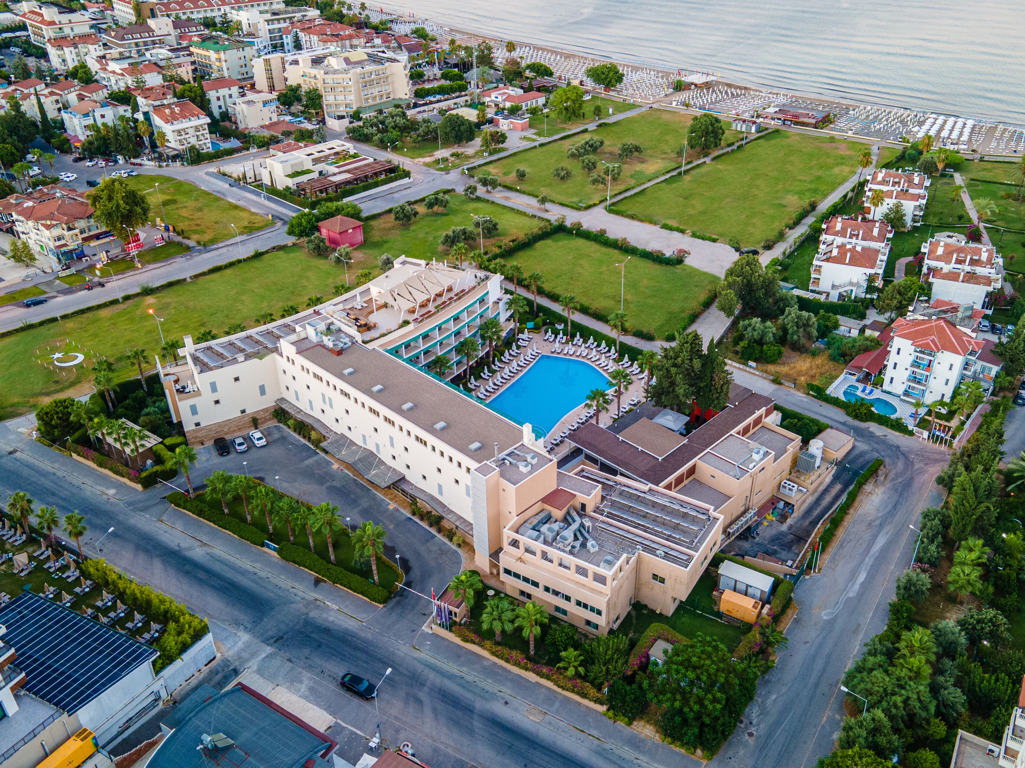 An aerial view of a hotel with a swimming pool, multiple floors, and a parking area.