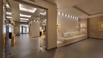 A spacious lobby with a reception desk, a seating area with a cushioned bench, and a decorative wall with recessed lighting.
