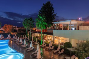A poolside area with lounge chairs and umbrellas, a restaurant, and a building with illuminated signage.