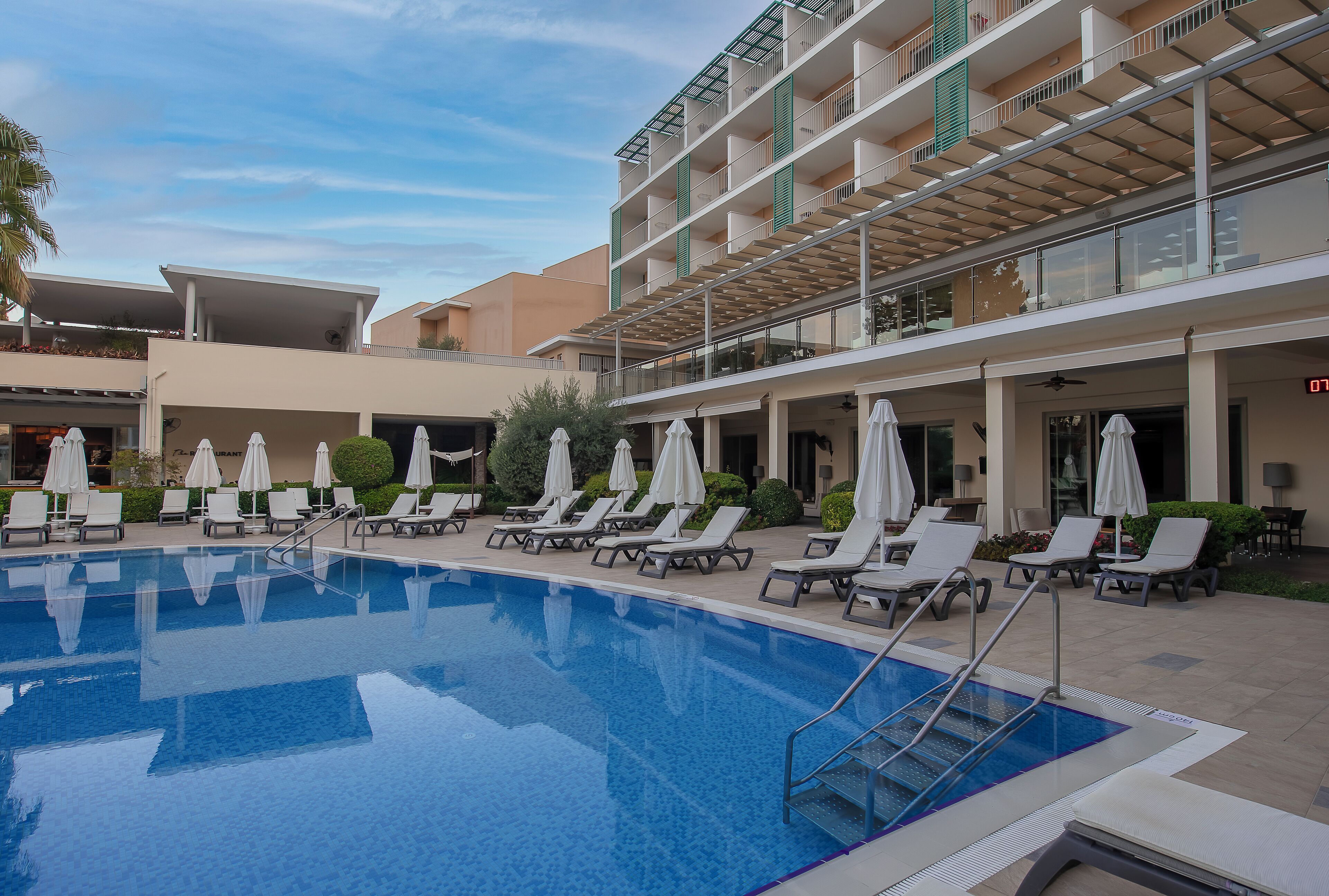 A swimming pool with lounge chairs and umbrellas, surrounded by a multi-story building with balconies.