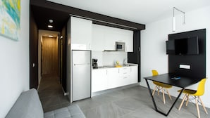 A modern kitchen with white cabinets, a black countertop, and a built-in microwave. There is a dining area with a black table and two yellow chairs.