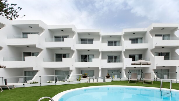 A modern hotel with a swimming pool, multiple balconies, and outdoor seating areas.