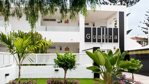 A hotel entrance with a sign reading "Guatiza," surrounded by potted plants and a white fence.