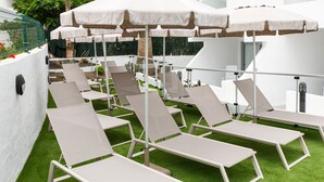 A rooftop terrace with multiple sun loungers and umbrellas.