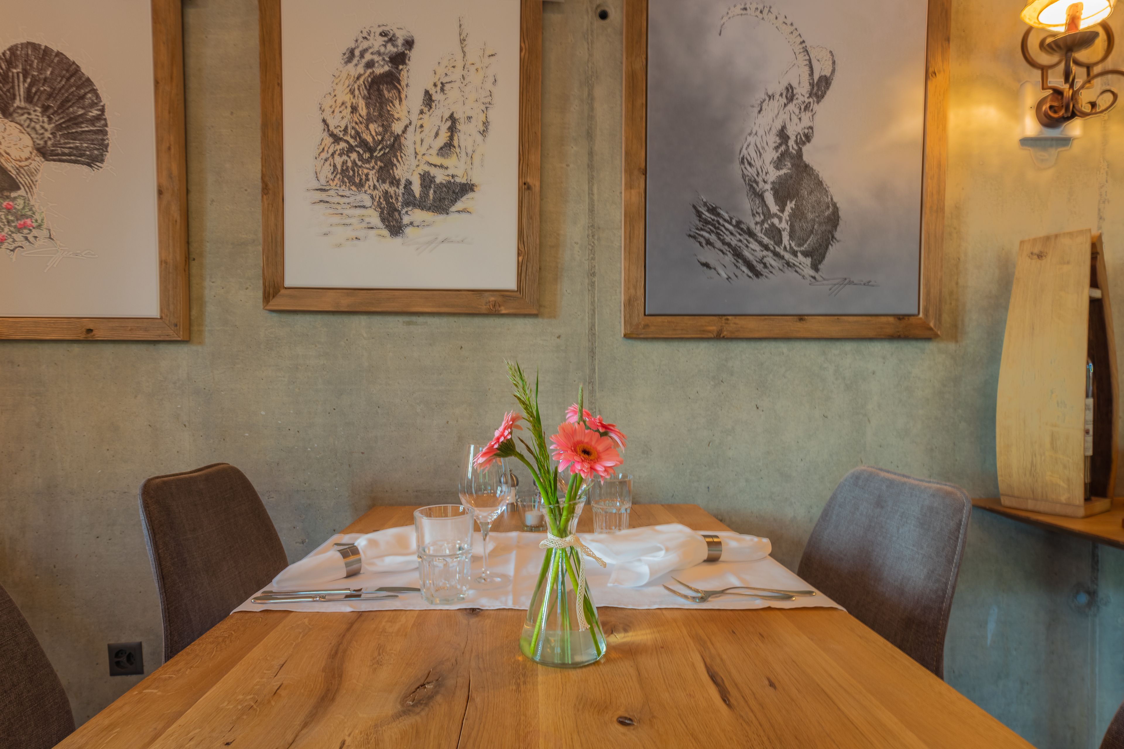 Ein Esstisch mit Blumen in einer Vase, Kunstwerk an der Wand und ein Holzstuhl.
