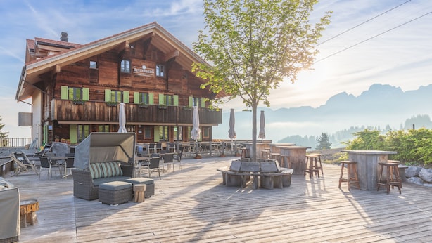 A wooden building with outdoor seating and a tree in the foreground.