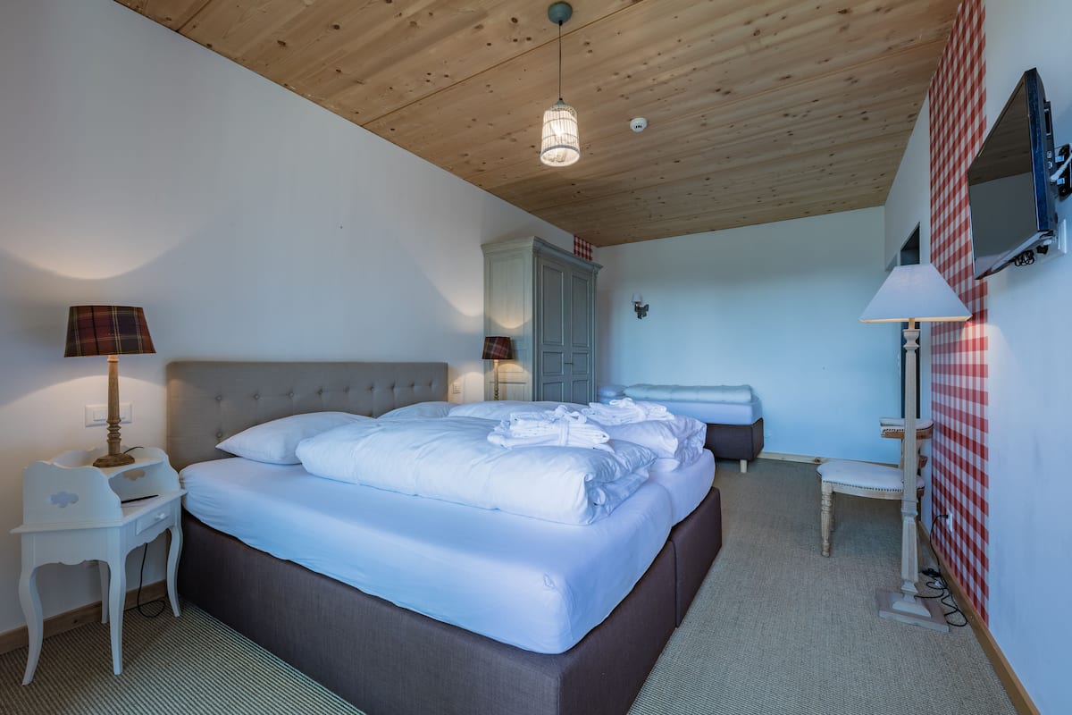 A bedroom with a large bed, bedside tables, a wardrobe, a mirror, and a television.
