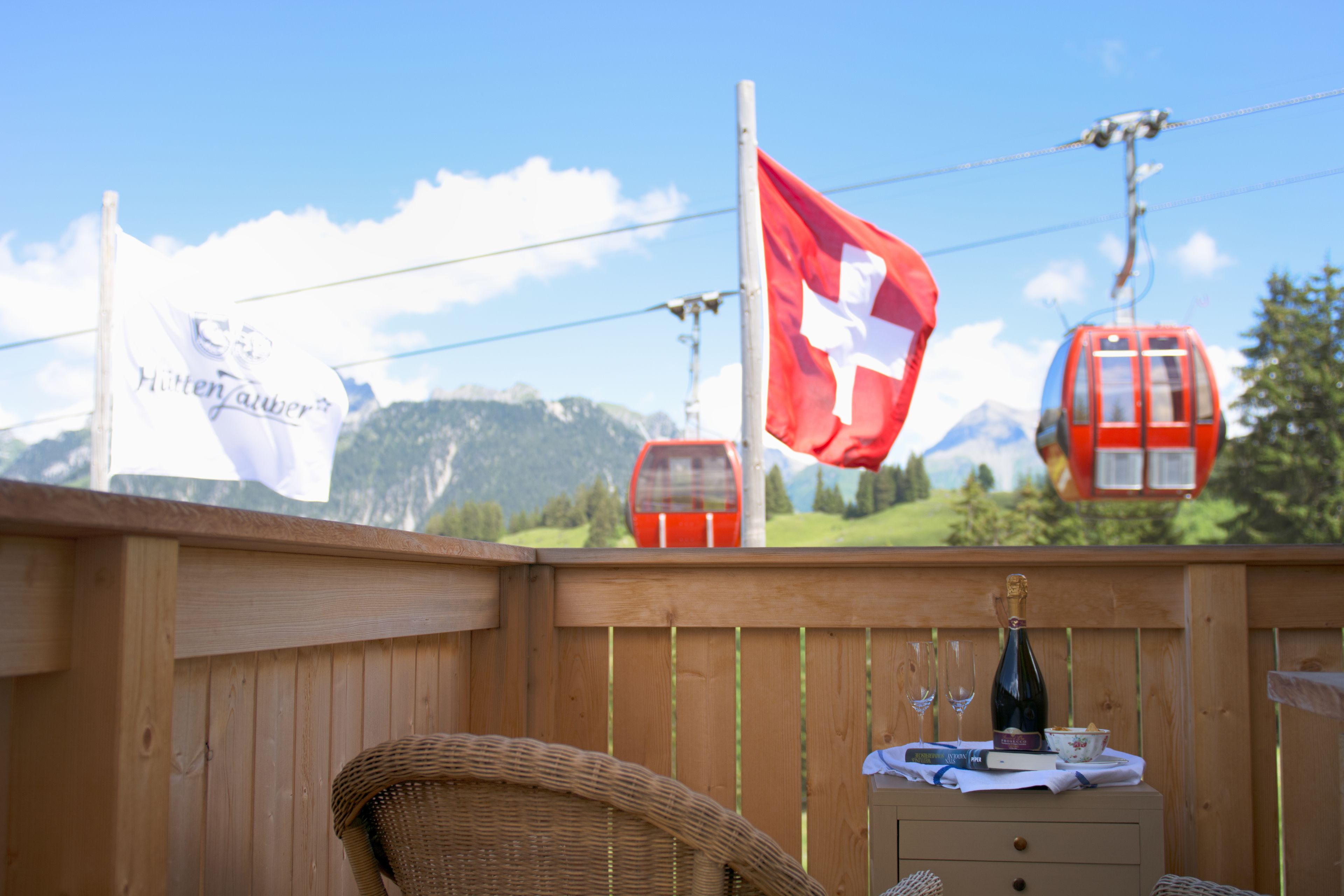 A wooden deck with a wicker chair and a small table with a bottle and glasses.