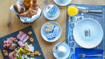 A breakfast setting with croissants, yogurt, and a variety of cheeses and meats on a slate board.