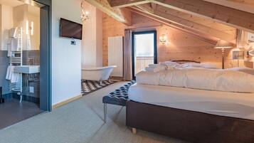 Ein Schlafzimmer mit Bett, einer Bank, einer Badewanne und einem Badezimmer inklusive Waschbecken und Handtuchhalter.