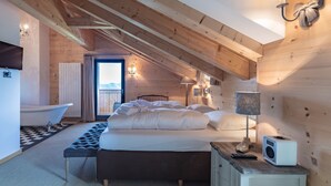 A bedroom with a large bed, a bathtub, and a wooden ceiling.