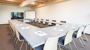 A conference room with a long table, chairs, a whiteboard, and a projector screen.