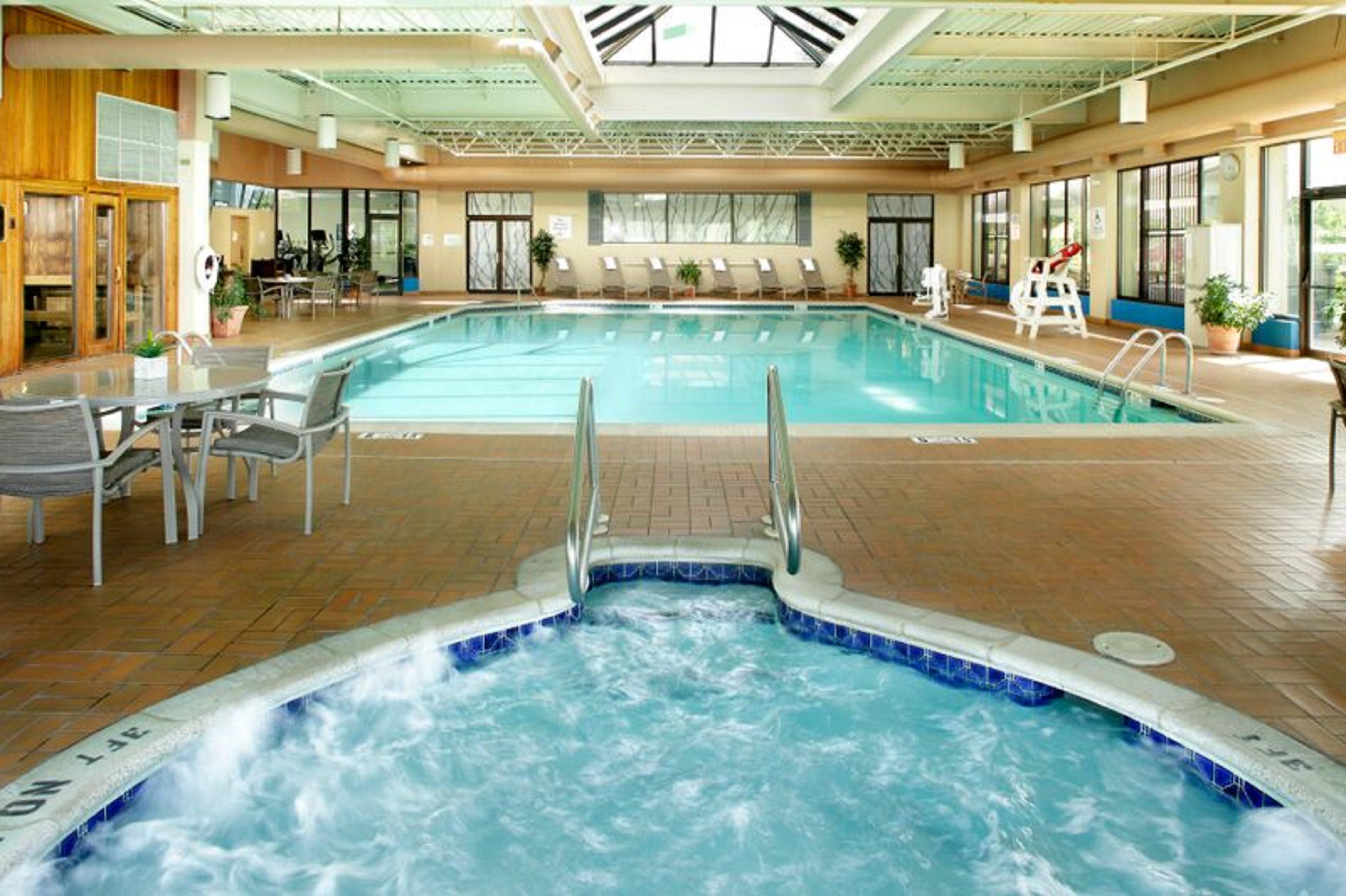 En indendørs swimmingpool med jacuzzi, liggestole og et ovenlys.