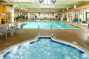 Una piscina interior con un jacuzzi, sillas de descanso y tragaluces.