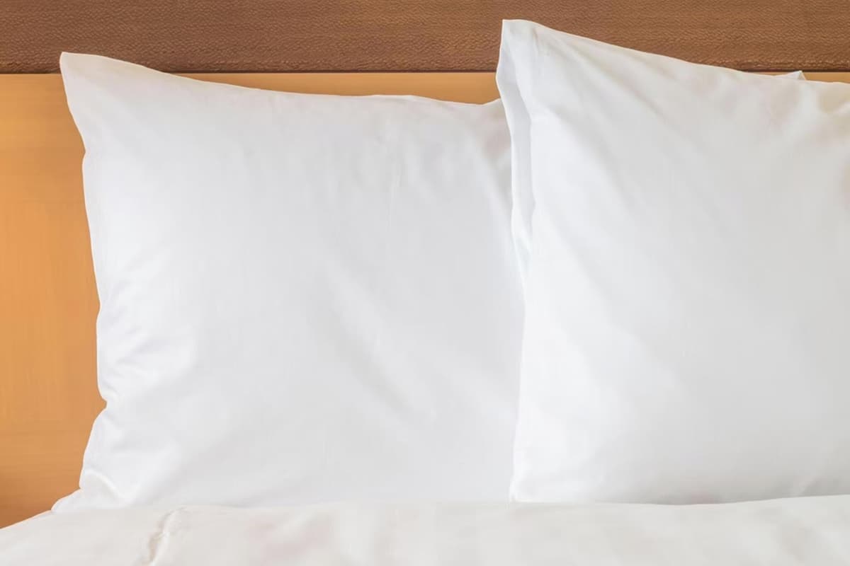 Una cama con ropa blanca y cabecera de madera.