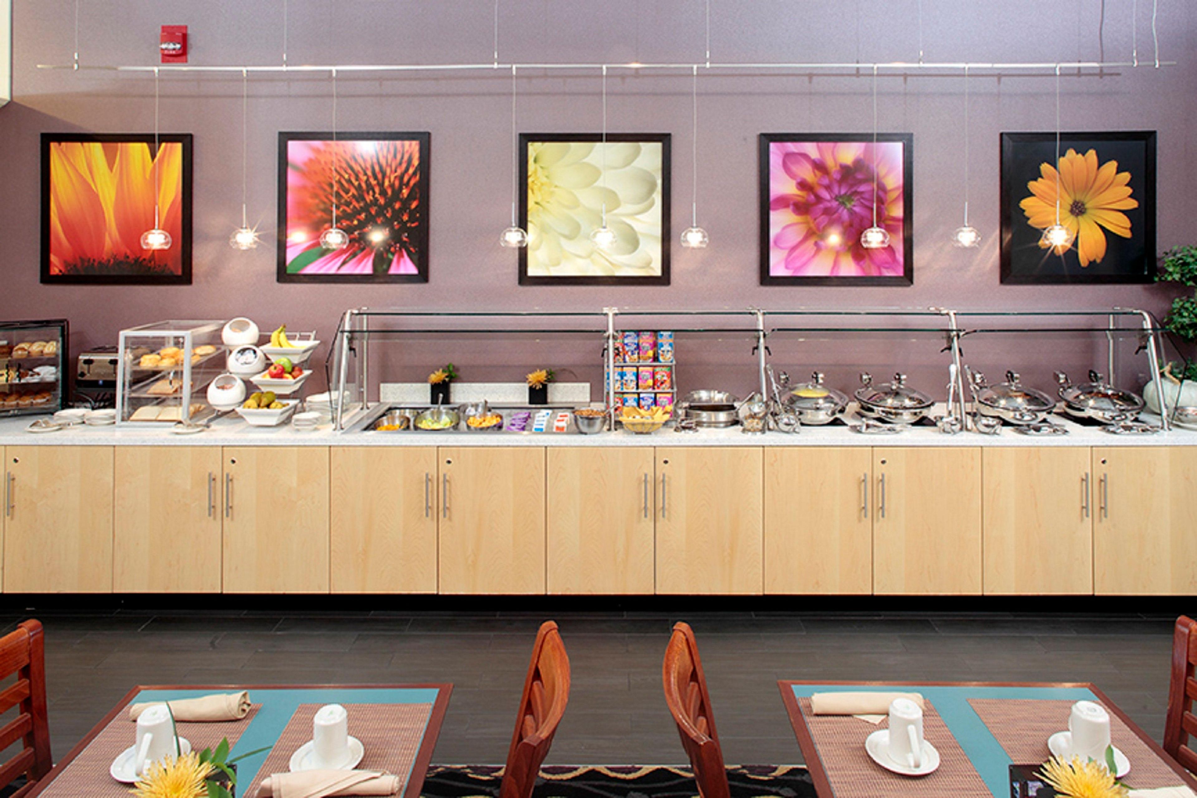 A buffet setup with various food items, a counter with kitchenware, and framed floral artwork on the wall.