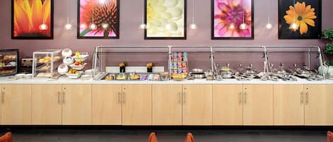 A buffet setup with various food items, a counter with kitchenware, and framed floral artwork on the wall.