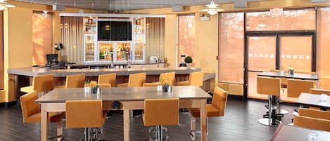 Ein Restaurant mit hohen Tischen und Stühlen, einer Bar und großen Fenstern.