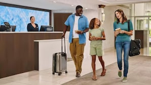 A hotel reception area with a digital screen, a reception desk, and a luggage cart. - Doubletree by Hilton Wilkes-barre (Wilkes-Barre)