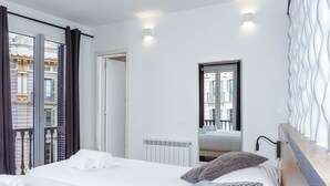 Ein Hotelzimmer mit Bett, zwei Kissen, einem fensterbepflanzten Fenster, einem Heizkörper und einem Spiegel, der den Raum reflektiert.