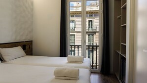 A hotel room with two beds, a wooden headboard, a balcony with a view of buildings, and a wardrobe. - Fontanella Green House (Barcelona)