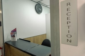 Un espace d’accueil comprenant un comptoir de réception, une horloge murale et un panneau indiquant le service d’accueil.