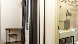 Ein Badezimmer mit Waschbecken, Spiegel und Toilette. Ein Stuhl und ein Fenster mit Vorhängen sind ebenfalls vorhanden.