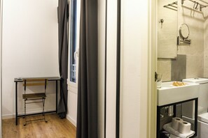 Une salle de bain avec un lavabo, un miroir et des toilettes. Il y a une chaise et une fenêtre avec des rideaux.