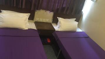 A small room with two beds, each with a purple bedspread and white pillows. There is a wooden nightstand between the beds with a red object on it.