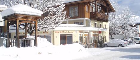 A two-story building with a wooden facade, a covered outdoor seating area, and a snow-covered street.
