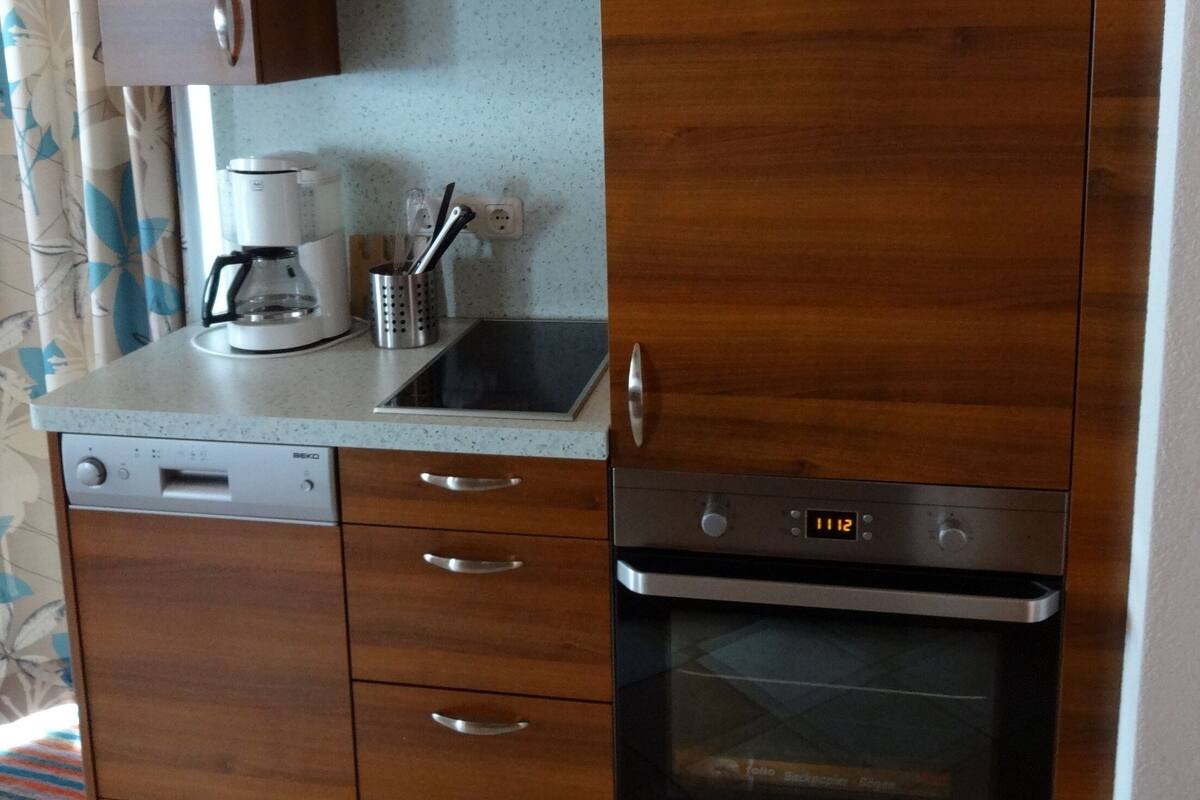 Une cuisine compacte dotée de meubles en bois, d’un lave-vaisselle, d’une machine à café et d’un four.