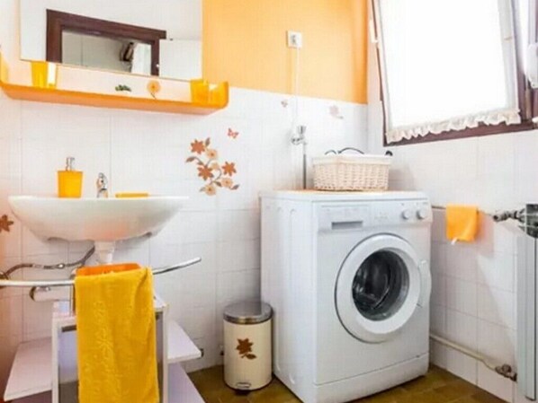 A compact bathroom with a white sink, a washing machine, and a small trash bin. - Apartment Palcic (Zadar)