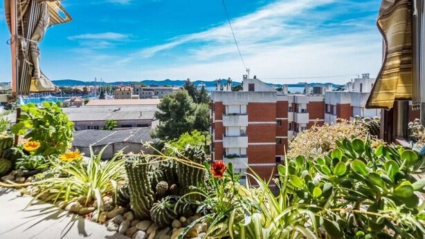 A terrace with potted plants, a view of a cityscape, and a building with a striped facade. - Apartment Palcic (Zadar)