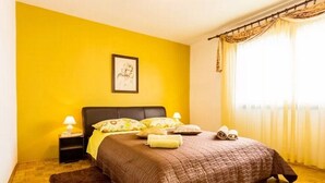 A bedroom with a bed, a nightstand, a lamp, a framed picture on the wall, and a window with curtains. - Apartment Palcic (Zadar)
