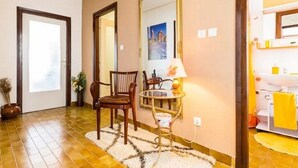 A hotel room with a wooden floor, a mirror, a chair, a small table with a lamp, and a bathroom with a yellow towel. - Apartment Palcic (Zadar)