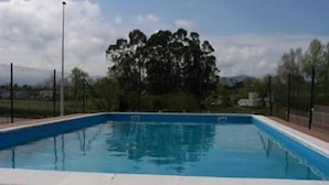 A rectangular swimming pool with a tiled deck, surrounded by a fence and trees.