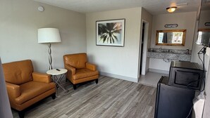 A compact living space with a sofa, a small table, a lamp, a framed picture, a kitchen area with a microwave, and a refrigerator. - Harmony Inn and Suites (Beaumont)