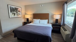 Ein Hotelzimmer mit einem Bett, zwei Nachttischen mit Lampen, einer Wand-Klimaanlage und einem Fenster mit Vorhängen.