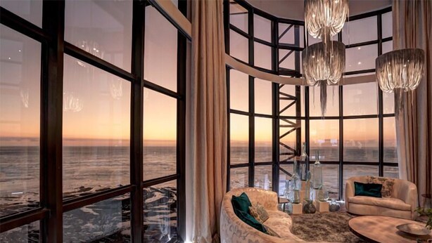 A modern living room with large floor-to-ceiling windows, a curved staircase, and a view of the ocean. - Ocean View Penthouse (Cape Town)