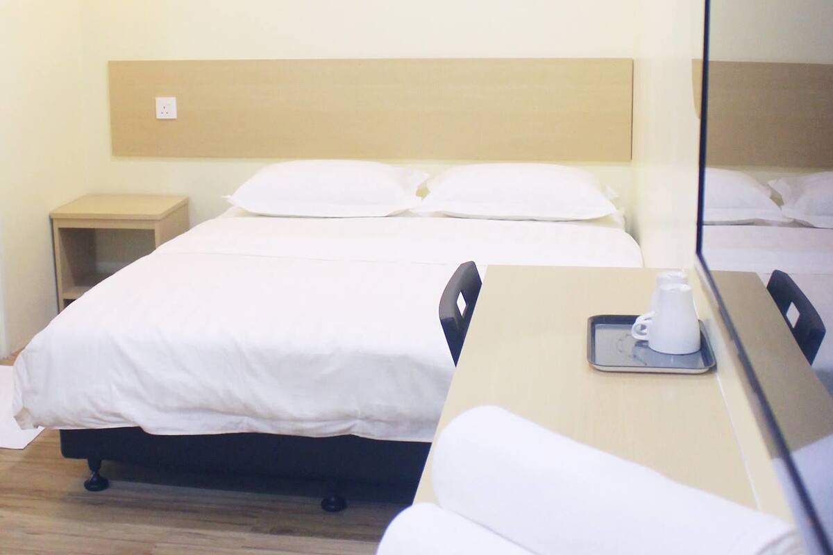 A hotel room with two beds, a bedside table with a cup and saucer, and a mirror.