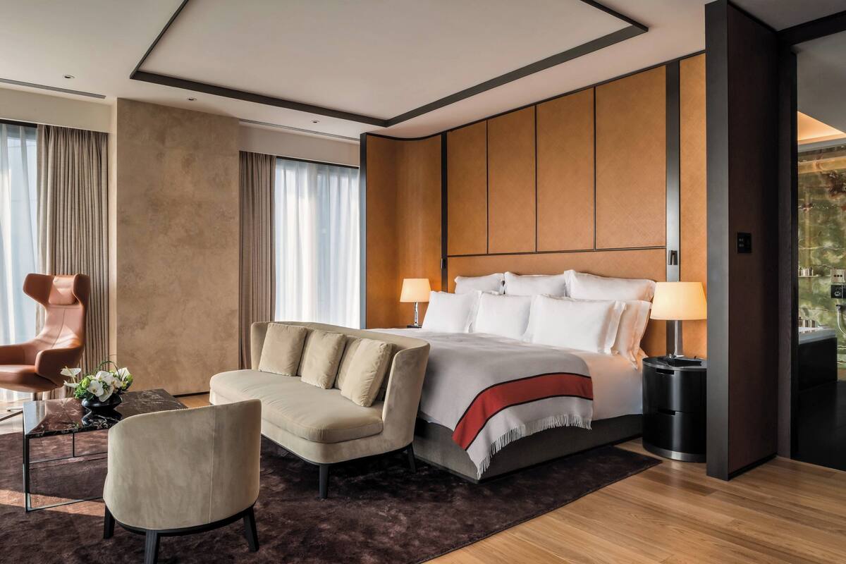 A modern hotel room with a large bed, a sofa, a chair, and a small table.
