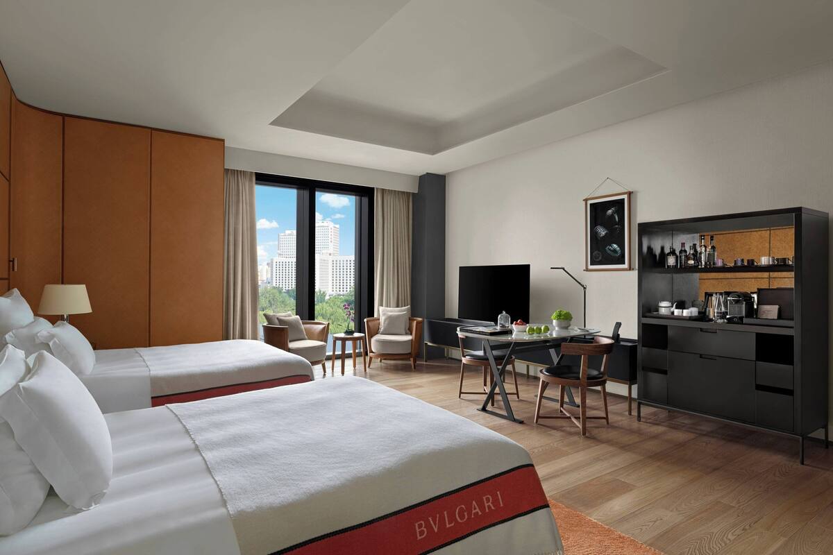 A hotel room with two beds, a desk, a chair, a TV, and a minibar.